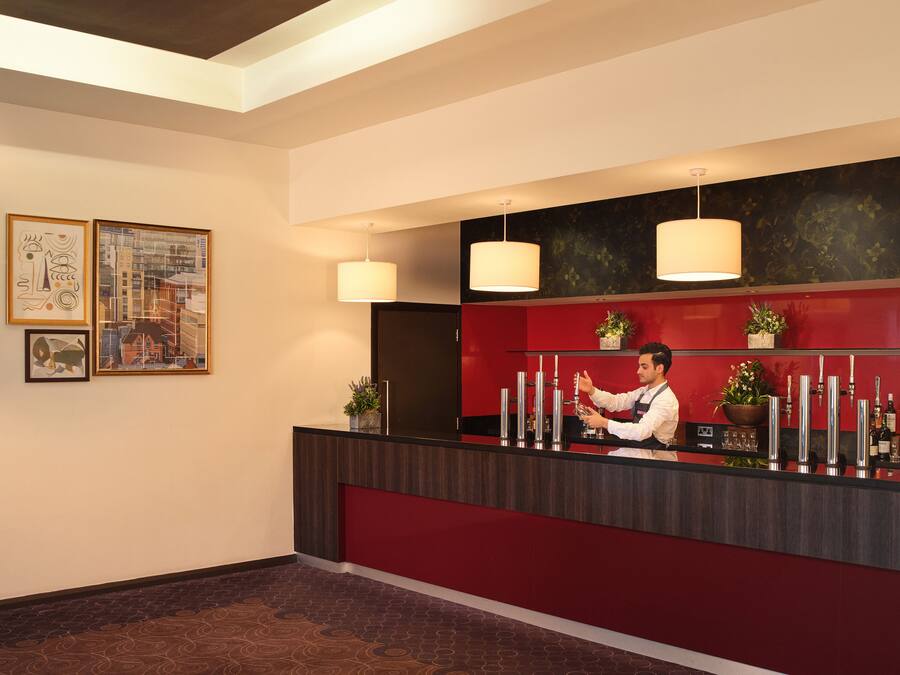 A hotel reception area with a red counter, multiple drink dispensers, and two hanging pendant lights.