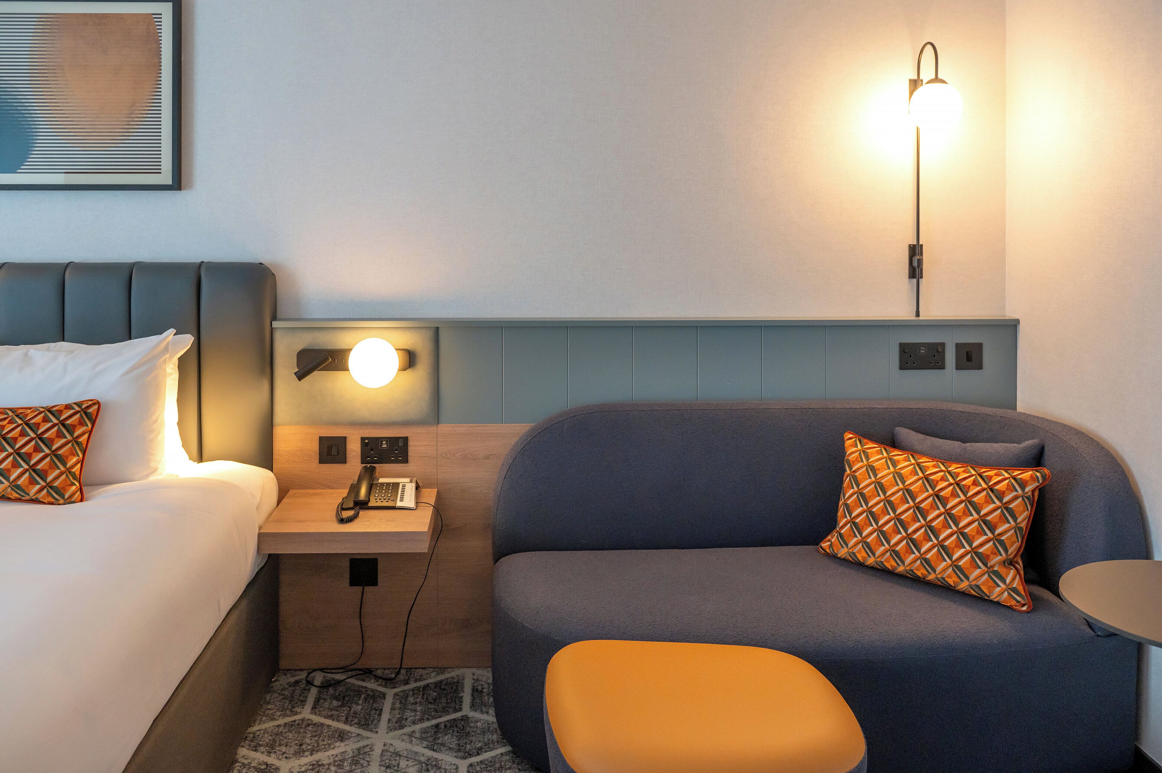 Een hotelkamer met een bed, een bureau met lamp, een bank en een klein tafeltje.