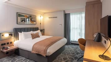 A hotel room with a bed, bedside table, lamp, chair, and a large window with curtains.