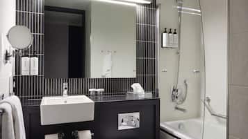Et moderne badeværelse med et sort-hvidt flisemønster, et stort spejl, en hvid vask, et toilet og en brusekabine med glasvægge.