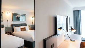 Een hotelkamer met twee bedden, een bureau, een stoel, een bureaulamp, een ingelijst schilderij aan de muur, en een raam met gordijnen.