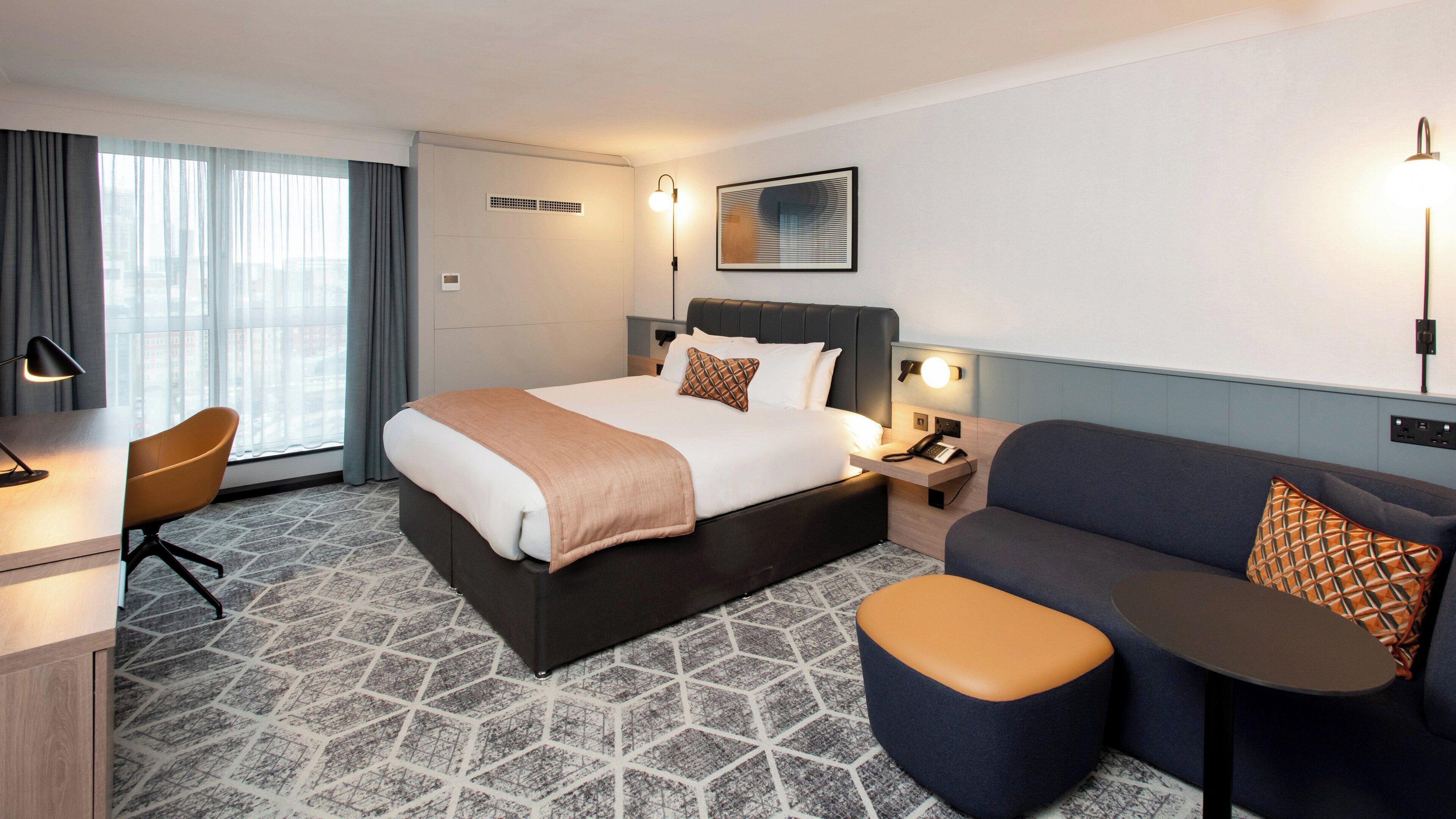 A hotel room with a large bed, a desk, a sofa, and a small table.