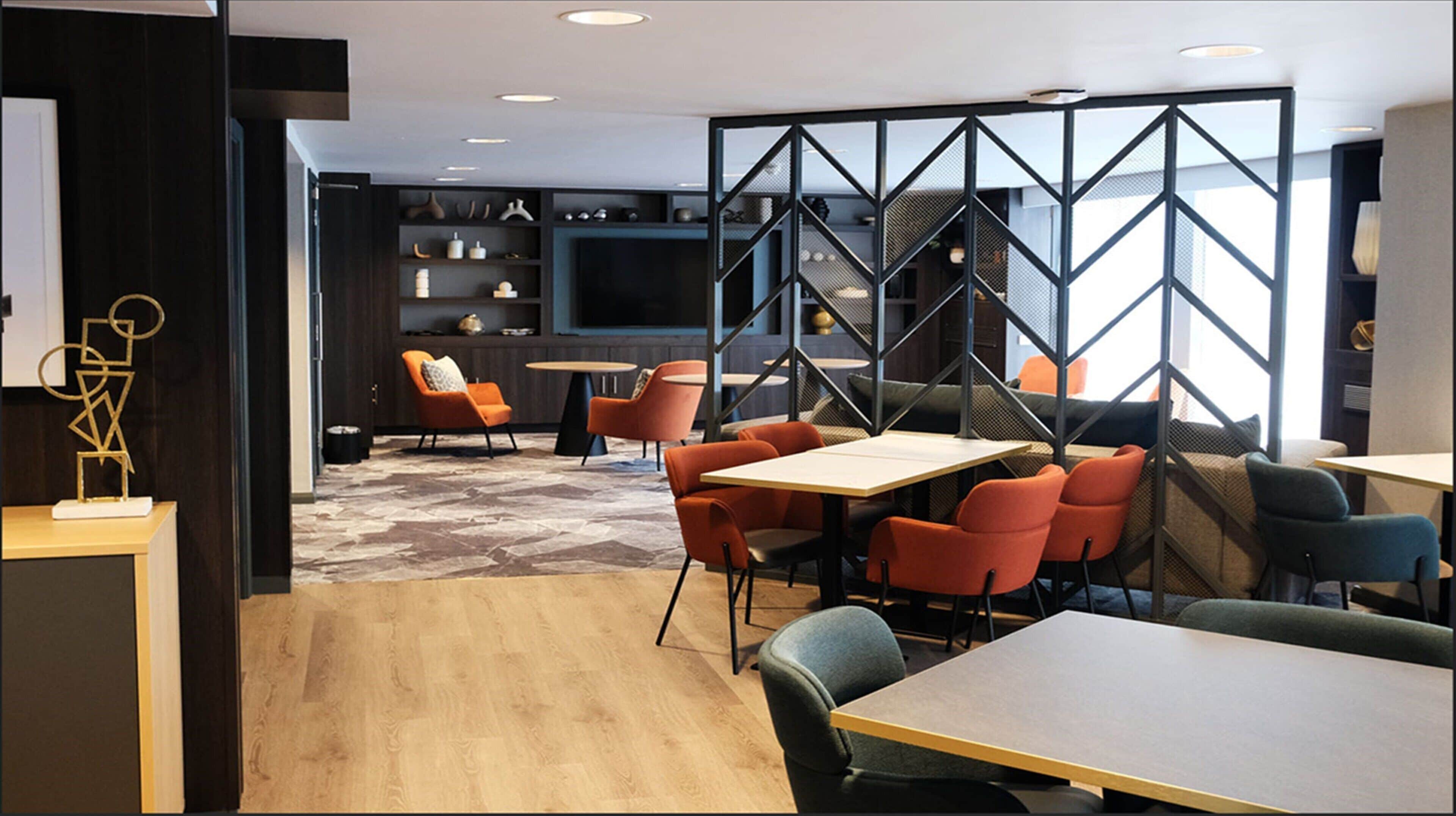 A modern lounge area with a mix of seating options, including tables and chairs, and a large screen wall.