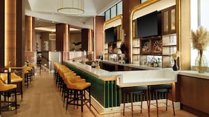 Zona de bar moderna con una barra larga, varios taburetes y estanterías llenas de botellas.