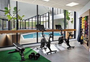 Un gimnasio con bicicletas estáticas, una banca, mancuernas y vistas a una piscina.