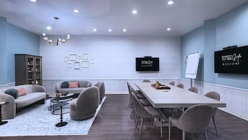 Una sala riunioni moderna con un lungo tavolo, sedute confortevoli, un lampadario e uno schermo TV che mostra un messaggio di benvenuto.