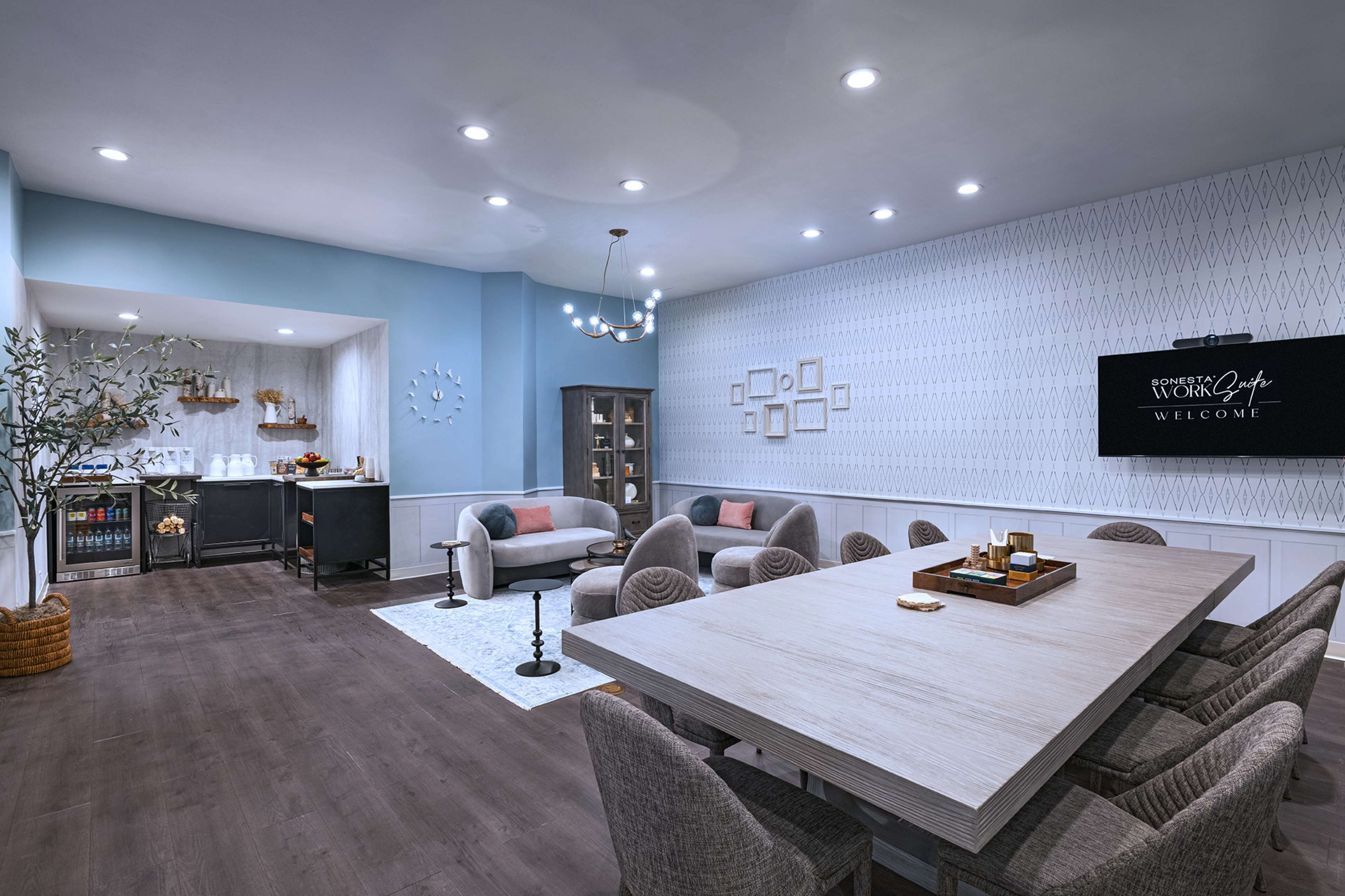 Un espace repas moderne avec une longue table, des chaises rembourrées et un écran de télévision fixé au mur.