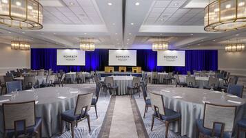 A conference room with round tables, chairs, and a stage with a blue curtain backdrop.
