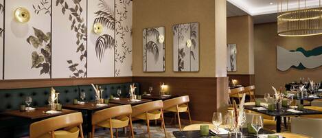 A restaurant with multiple tables and chairs, a patterned wall, and a modern chandelier.