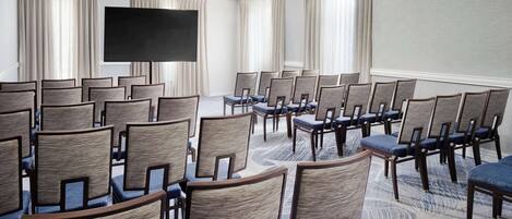 A conference room with rows of chairs, a large screen, and curtains.