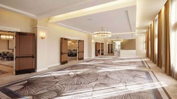 Un amplio vestíbulo de hotel con alfombra estampada, candelabros y vistas al comedor.