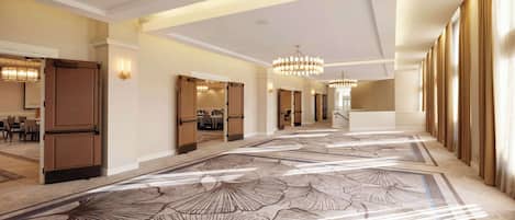 Un amplio vestíbulo de hotel con alfombra estampada, candelabros y vistas al comedor.