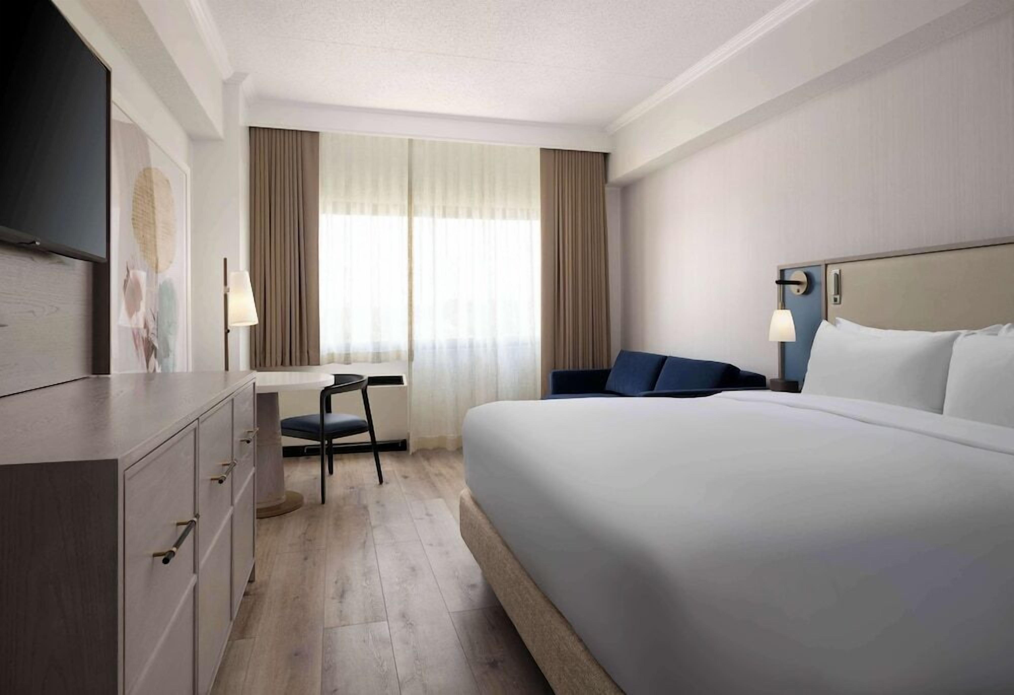 A hotel room with a bed, a desk, a chair, and a television.