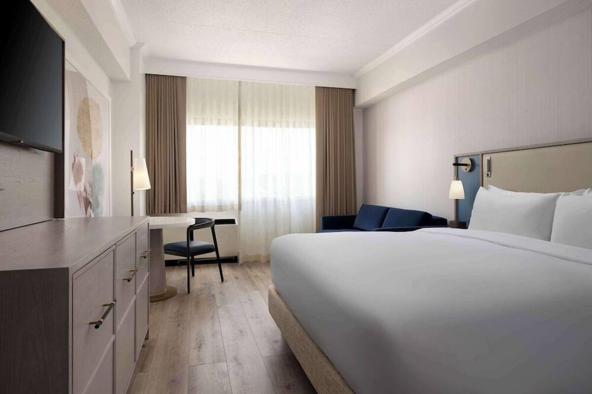 A hotel room with a bed, a desk, a chair, and a television.