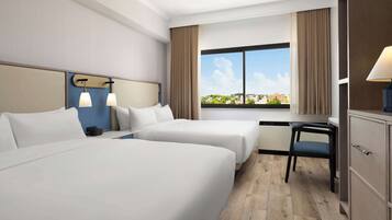 A hotel room with two beds, a desk, a chair, and a view of the city.