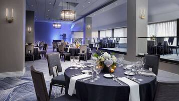 A dining area with round tables set for service, featuring a central floral arrangement and a modern chandelier.