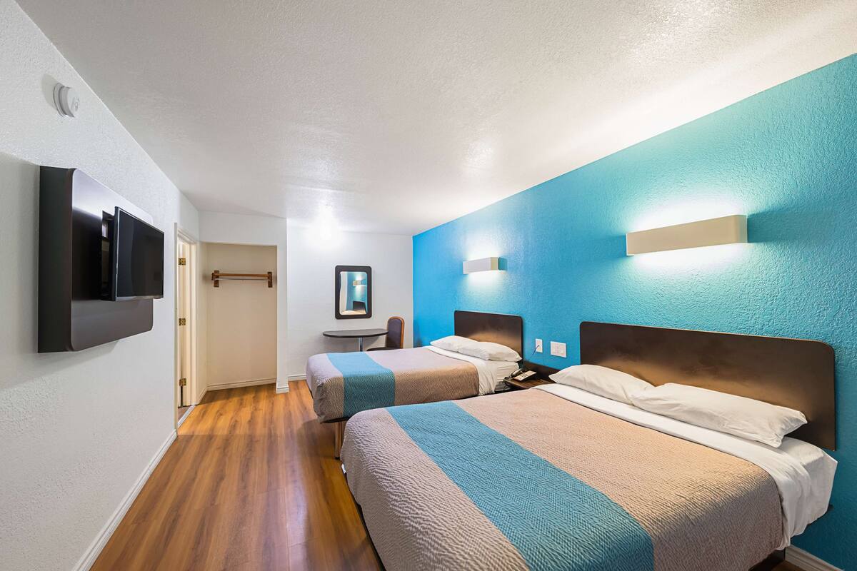 A hotel room with two beds, a TV mounted on the wall, a small table, and a mirror.