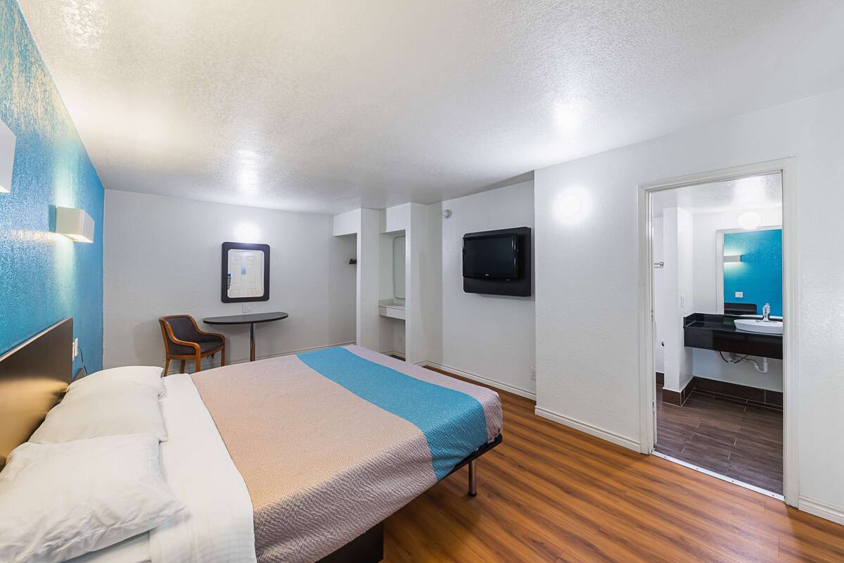 A hotel room with a bed, a desk, a chair, a television, and a bathroom visible through an open door.