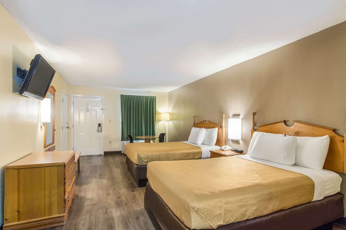 A hotel room with two beds, a wooden dresser, a television mounted on the wall, and a green curtain.