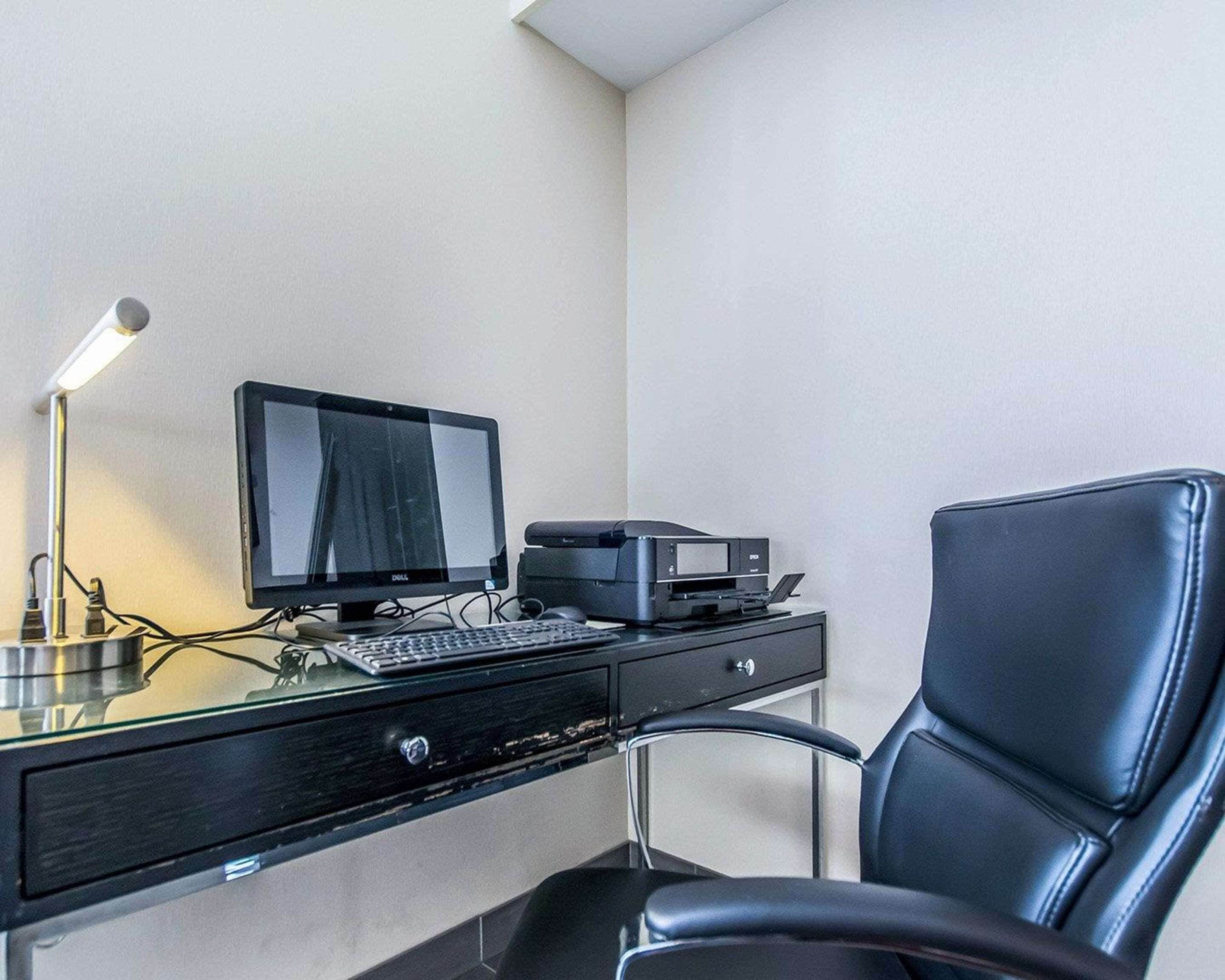 Habitación de hotel con escritorio, computadora, impresora y una silla de cuero negro.