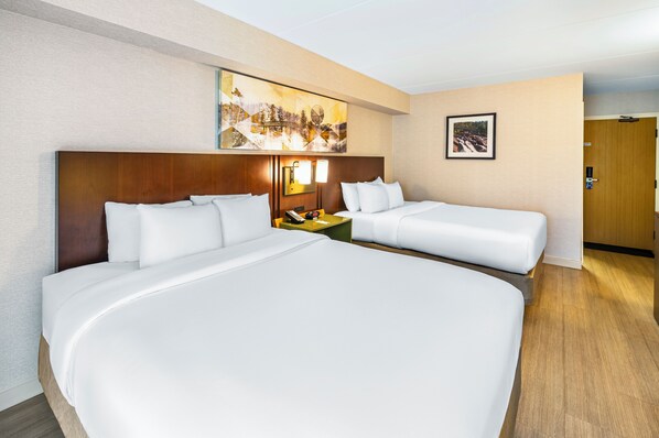 Quarto de hotel com duas camas, uma mesa de cabeceira com abajur e um quadro na parede.