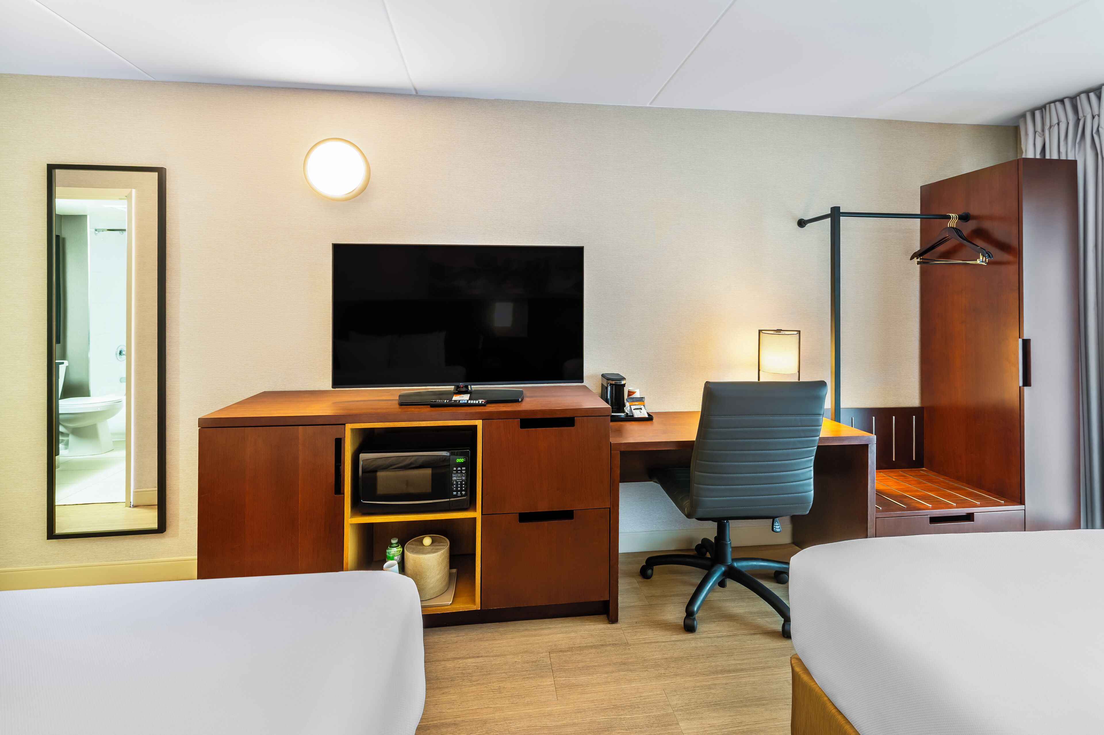 A hotel room with a wooden desk, a television, a chair, a bed, and a bathroom visible through an open door.