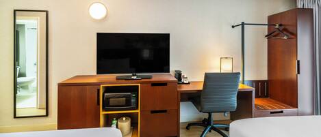 A hotel room with a wooden desk, a television, a chair, a bed, and a bathroom visible through an open door.