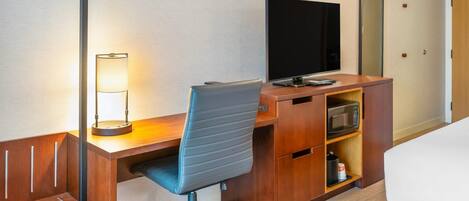 Une chambre d’hôtel équipée d’un bureau en bois, d’une chaise, d’une télévision, d’un four à micro-ondes et d’un lit.