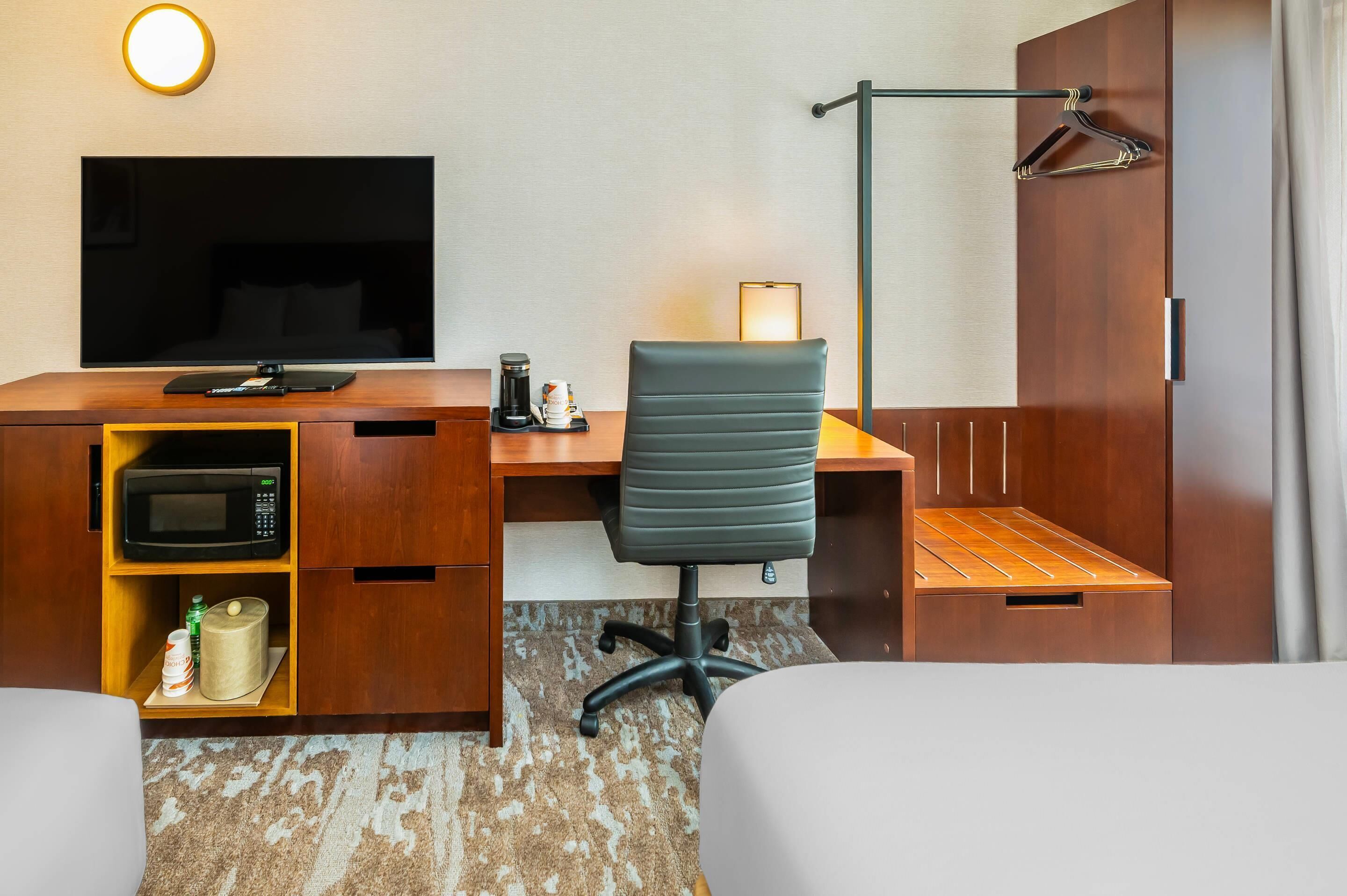 Una camera d'albergo con televisione a schermo piatto, una scrivania con macchina del caffè, una sedia e un letto.