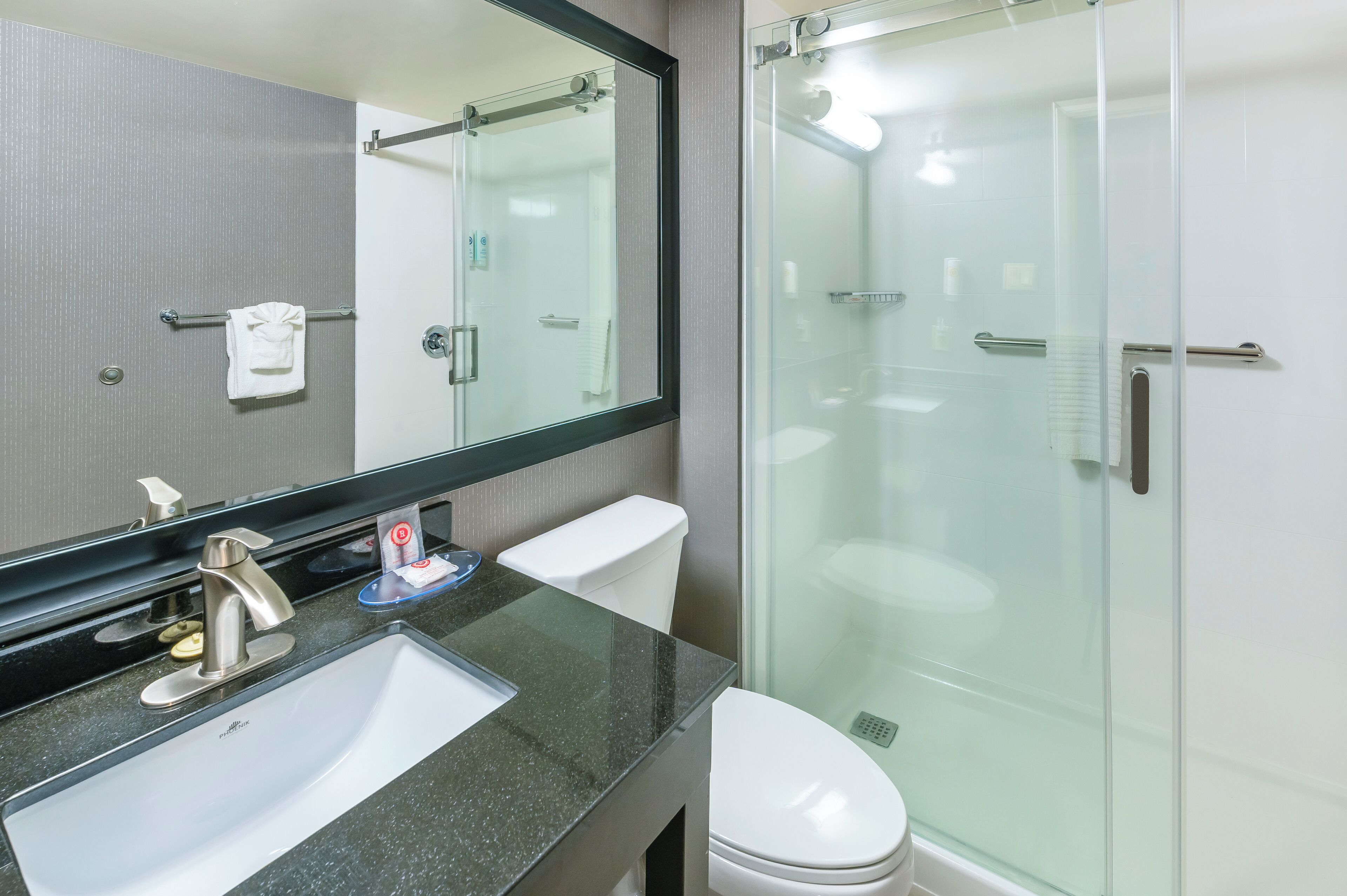 A modern bathroom with a glass-enclosed shower, a white toilet, and a sink with a black countertop.