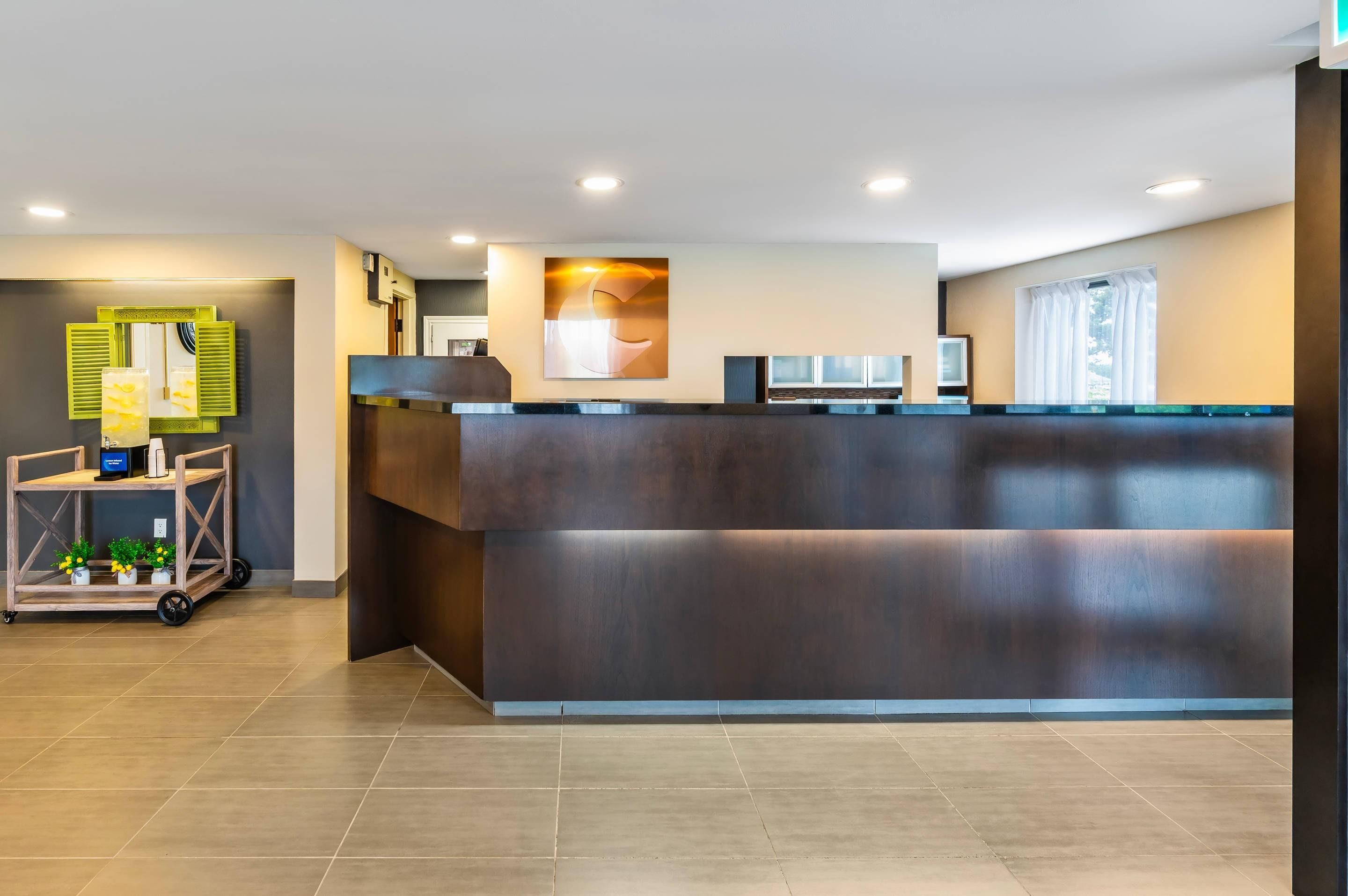 A reception desk with a digital display, a cart with small plants, and a wall-mounted artwork.