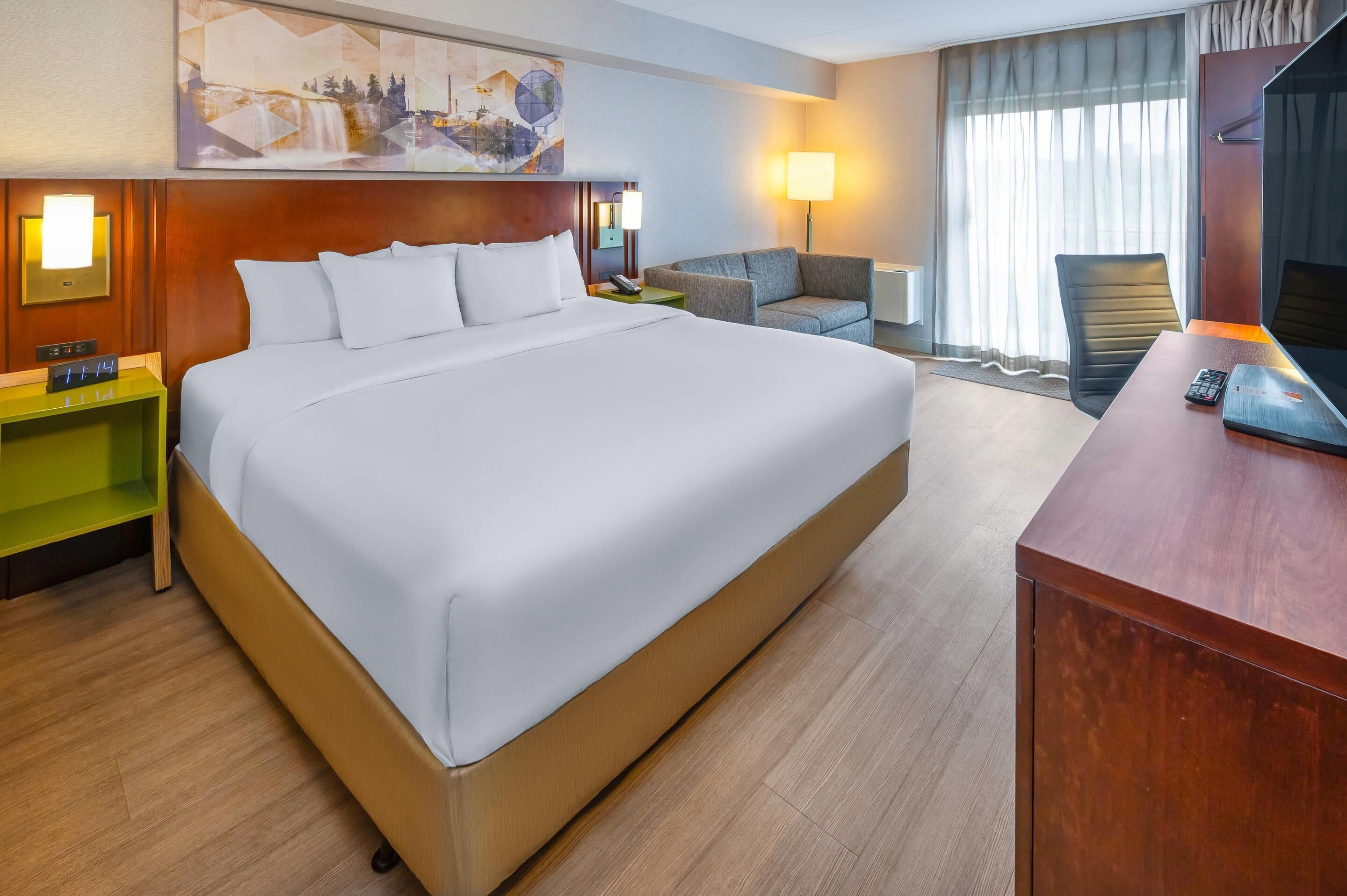 A hotel room with a large bed, a desk with a chair, a television, and a painting on the wall.
