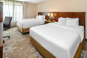 A hotel room with two beds, a desk, a chair, and a nightstand with a phone.