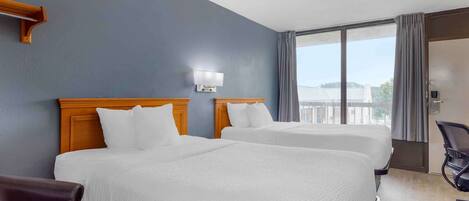 Une chambre d’hôtel avec deux lits, un bureau, une chaise et une grande fenêtre donnant sur un beau paysage.