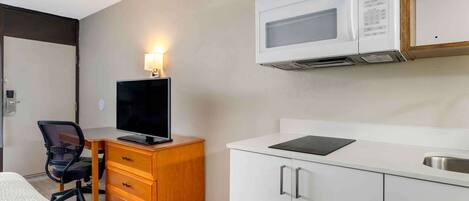 Habitación de hotel pequeña con cama, escritorio con computadora, televisor, microondas y kitchenette con lavamanos.
