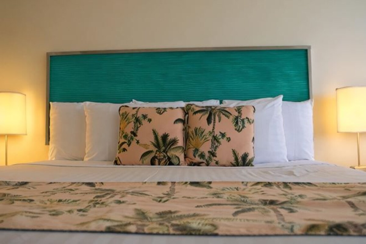 A bed with a teal headboard, white pillows, and a floral bedspread.
