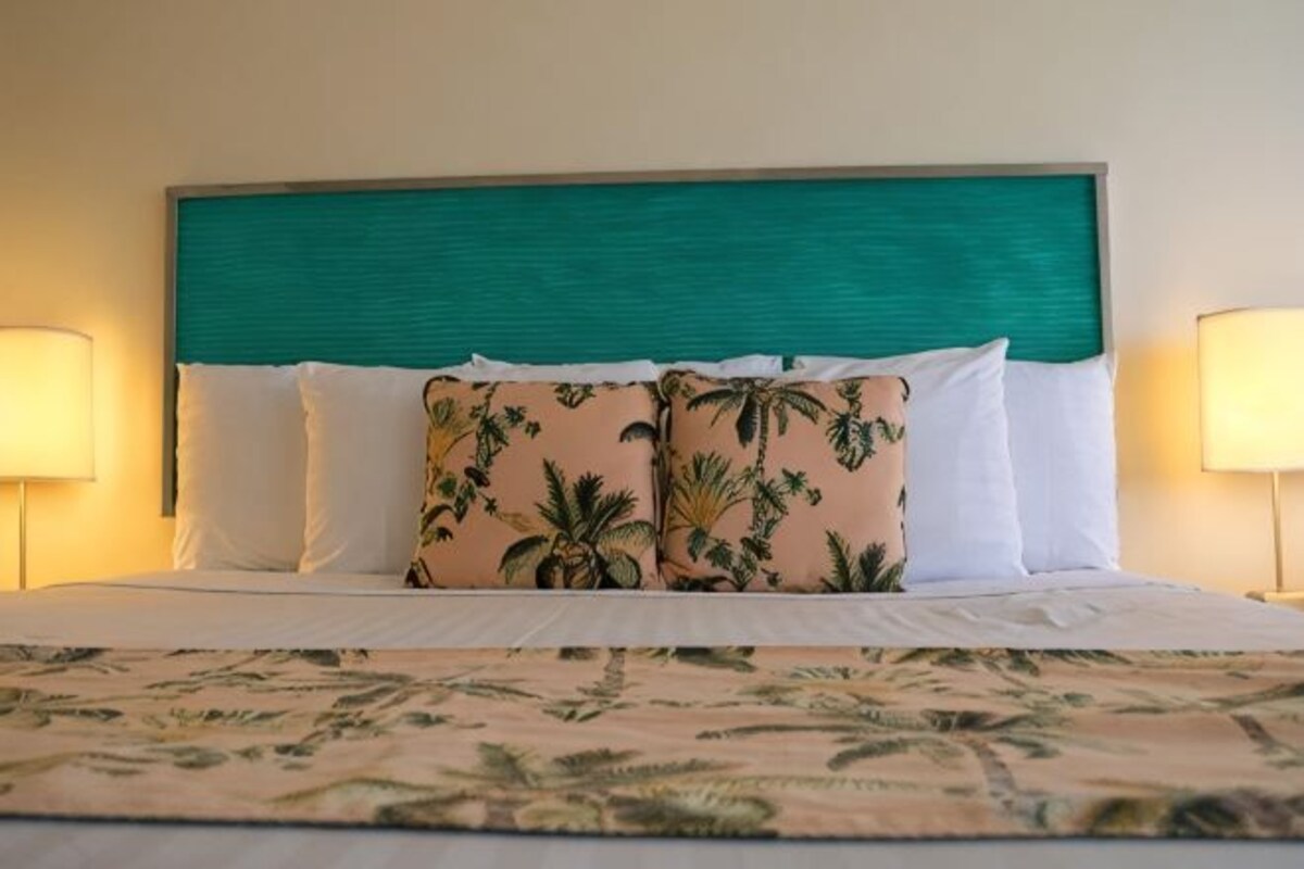A hotel room with a bed, a teal headboard, and two bedside lamps.