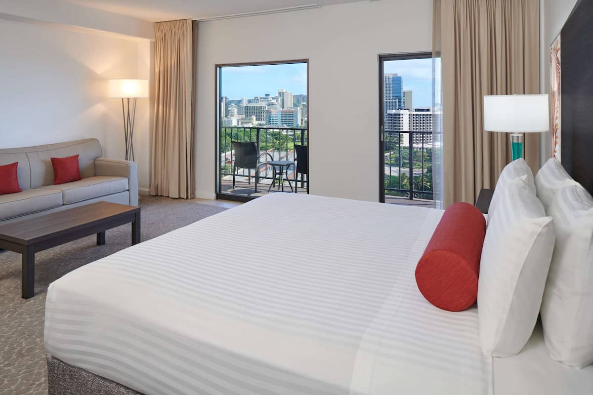 Une chambre d’hôtel avec un grand lit, un canapé, une table basse et un balcon offrant une vue sur la ville.