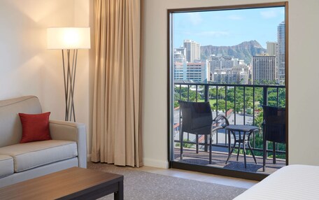 A hotel room with a balcony, a sofa, a lamp, and a view of the cityscape.