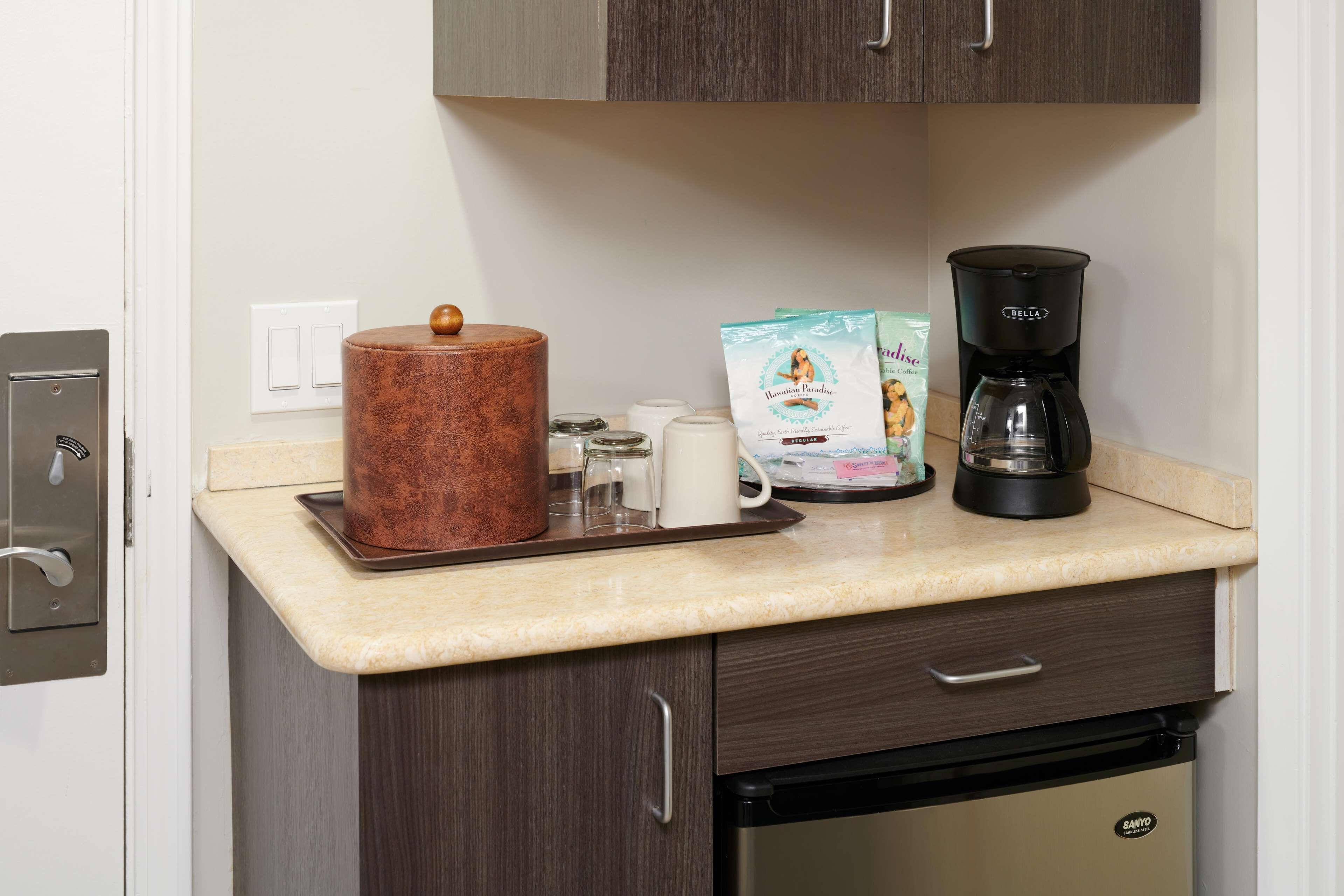 Eine Küche mit einer Arbeitsfläche, einer Kaffeemaschine, einer Kapselpackung Kaffee, einem Behälter und einem Kühlschrank.