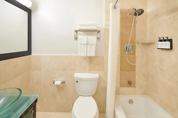 Ein Badezimmer mit Toilette, einem Waschbecken aus Glas, einer Dusche mit Duschbrausehandstück und einem Handtuchhalter mit gefalteten Handtüchern.