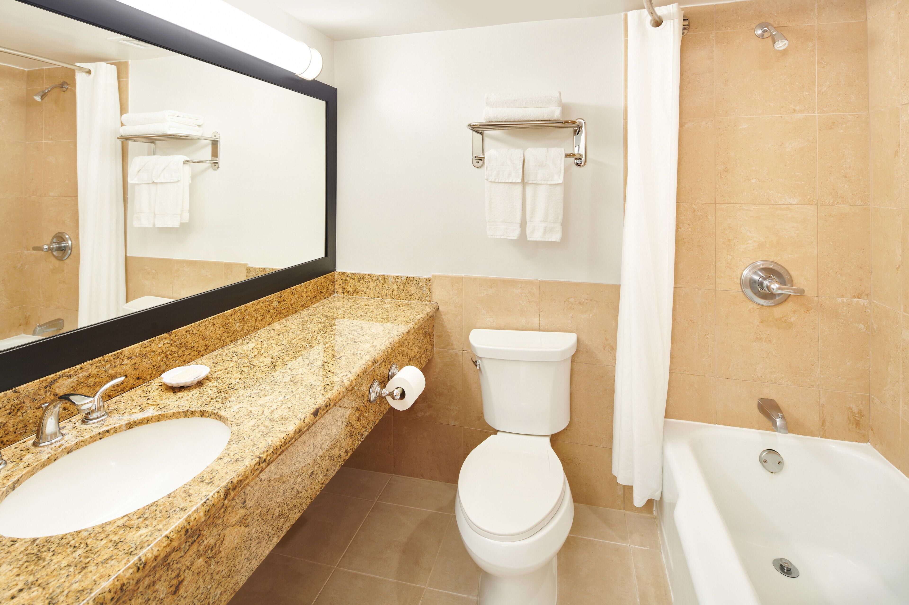 A bathroom with a granite countertop sink, a toilet, a bathtub, and a shower.