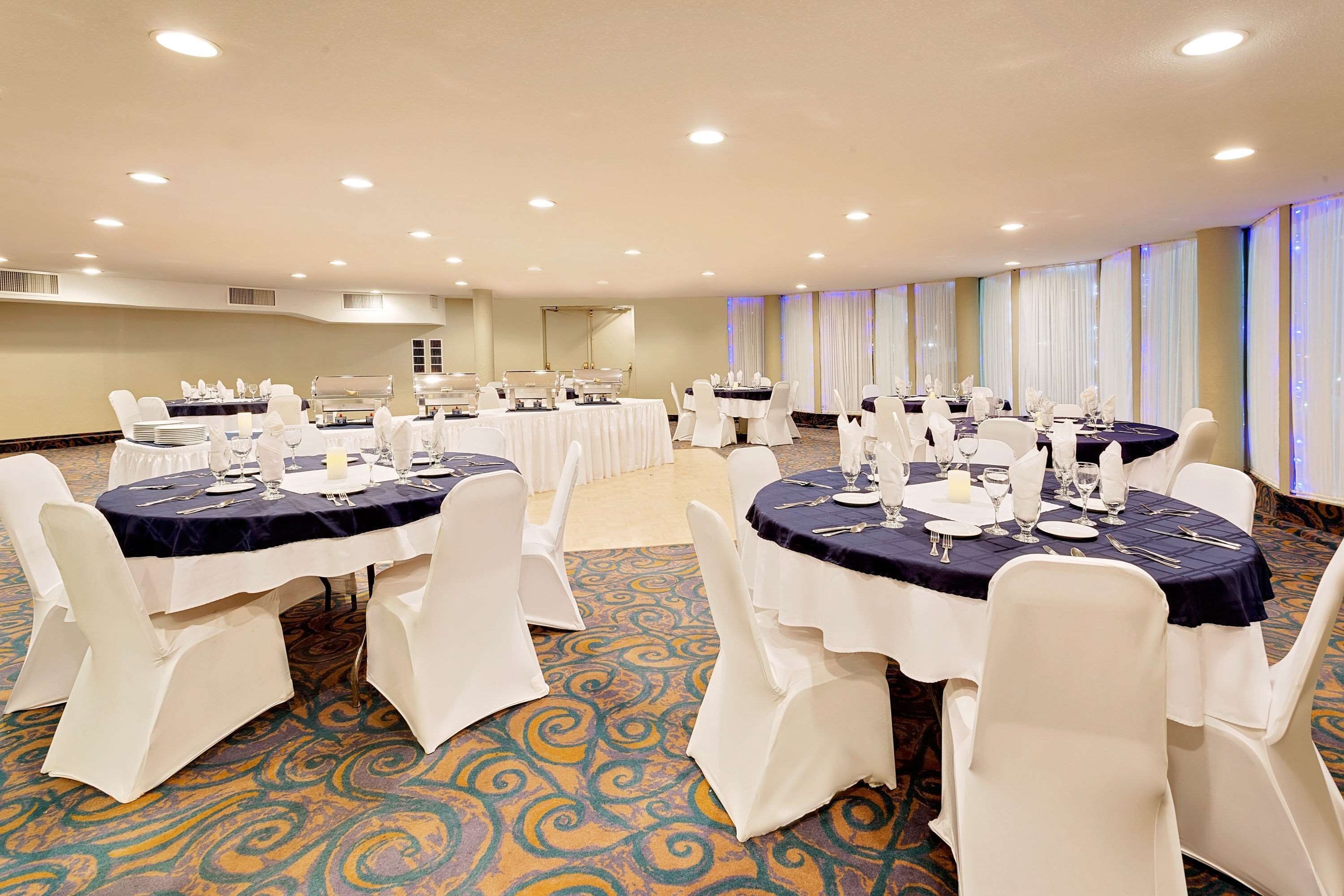 A conference room with round tables, white chairs, and a carpeted floor.