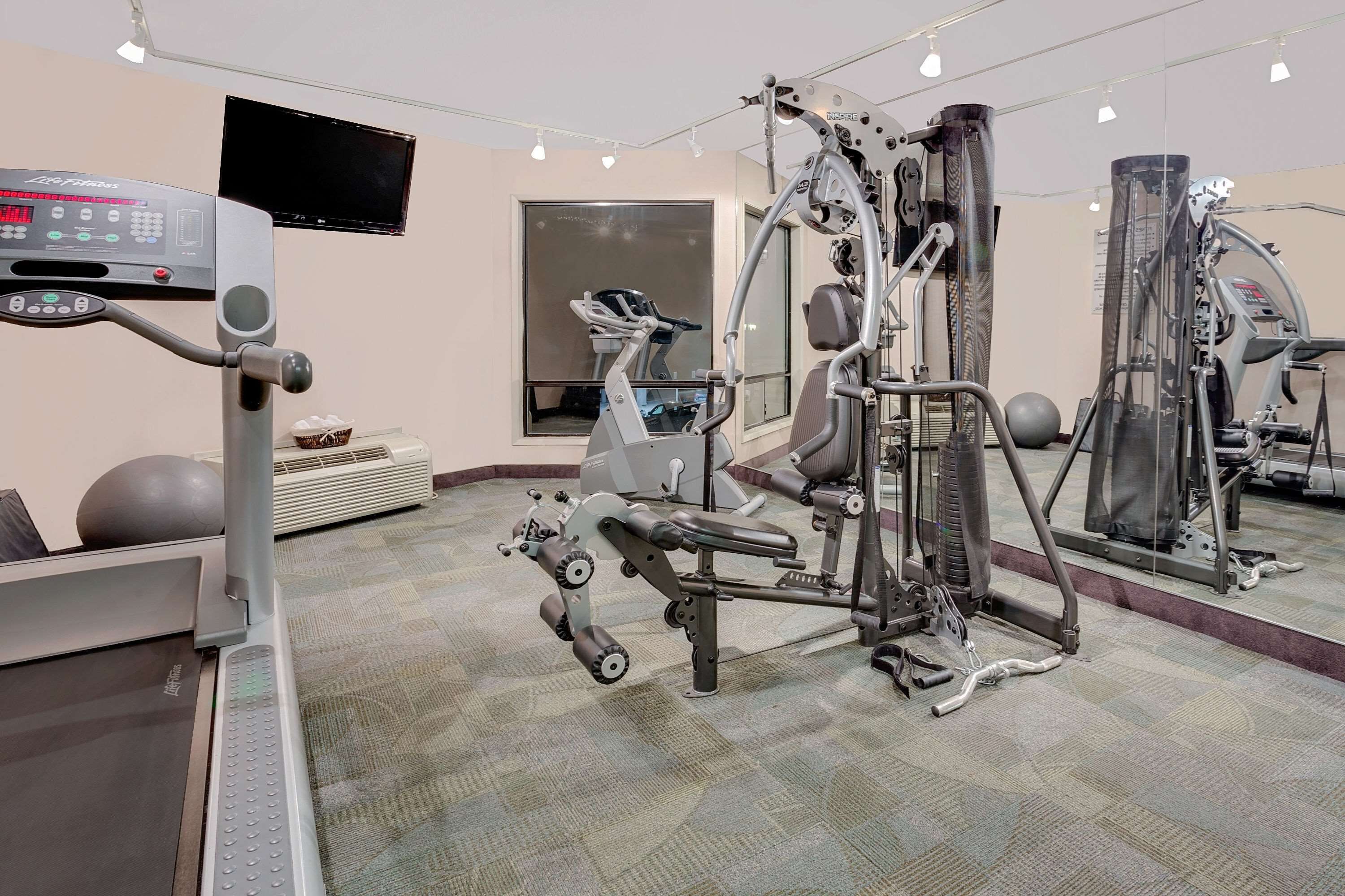 A gym with exercise equipment, a treadmill, and a television on the wall.