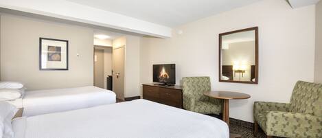 Habitación de hotel con dos camas, televisión, espejo y una mesita.