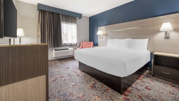 A hotel room with a large bed, a desk, a chair, a TV, and a window with curtains.