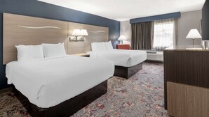 A hotel room with two beds, a desk, a chair, and a large window with curtains.