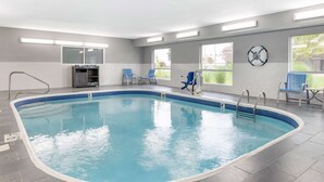 An indoor swimming pool with clear blue water, surrounded by grey tiled walls and a tiled floor. There are blue chairs and a small kitchenette area with a microwave and toaster. - Best Western Kokomo Hotel (Kokomo)