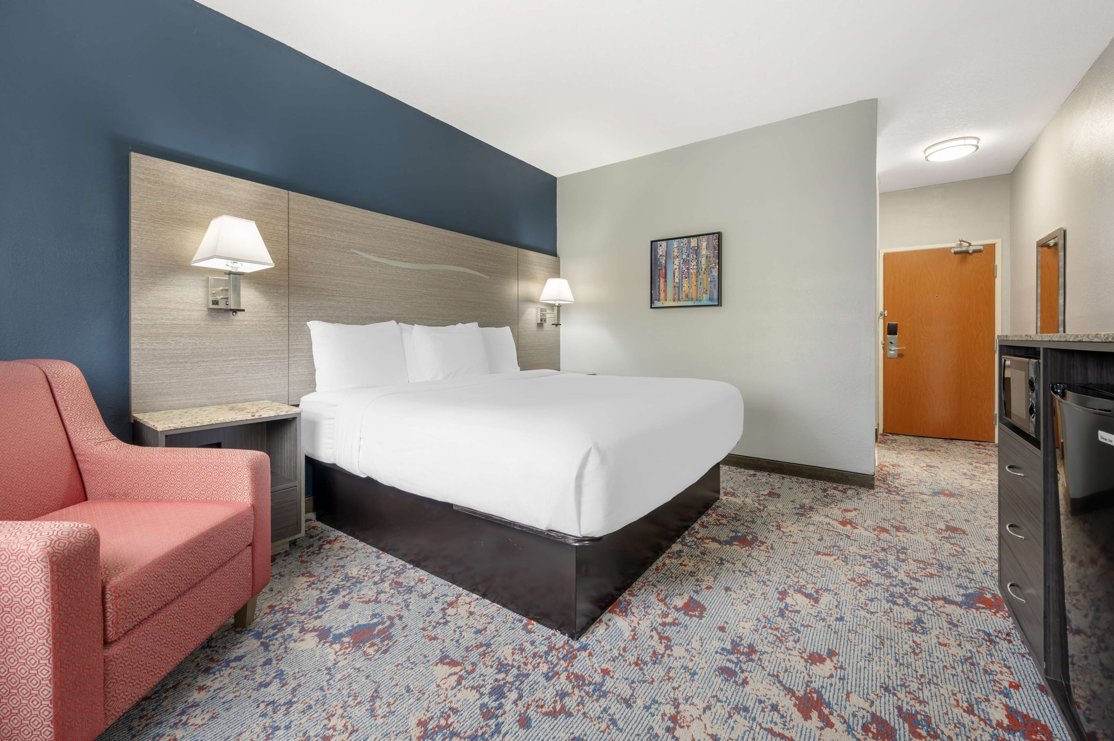 A hotel room with a large bed, a desk with a lamp, a chair, and a dresser.