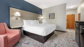 A hotel room with a large bed, a desk with a lamp, a chair, and a dresser.